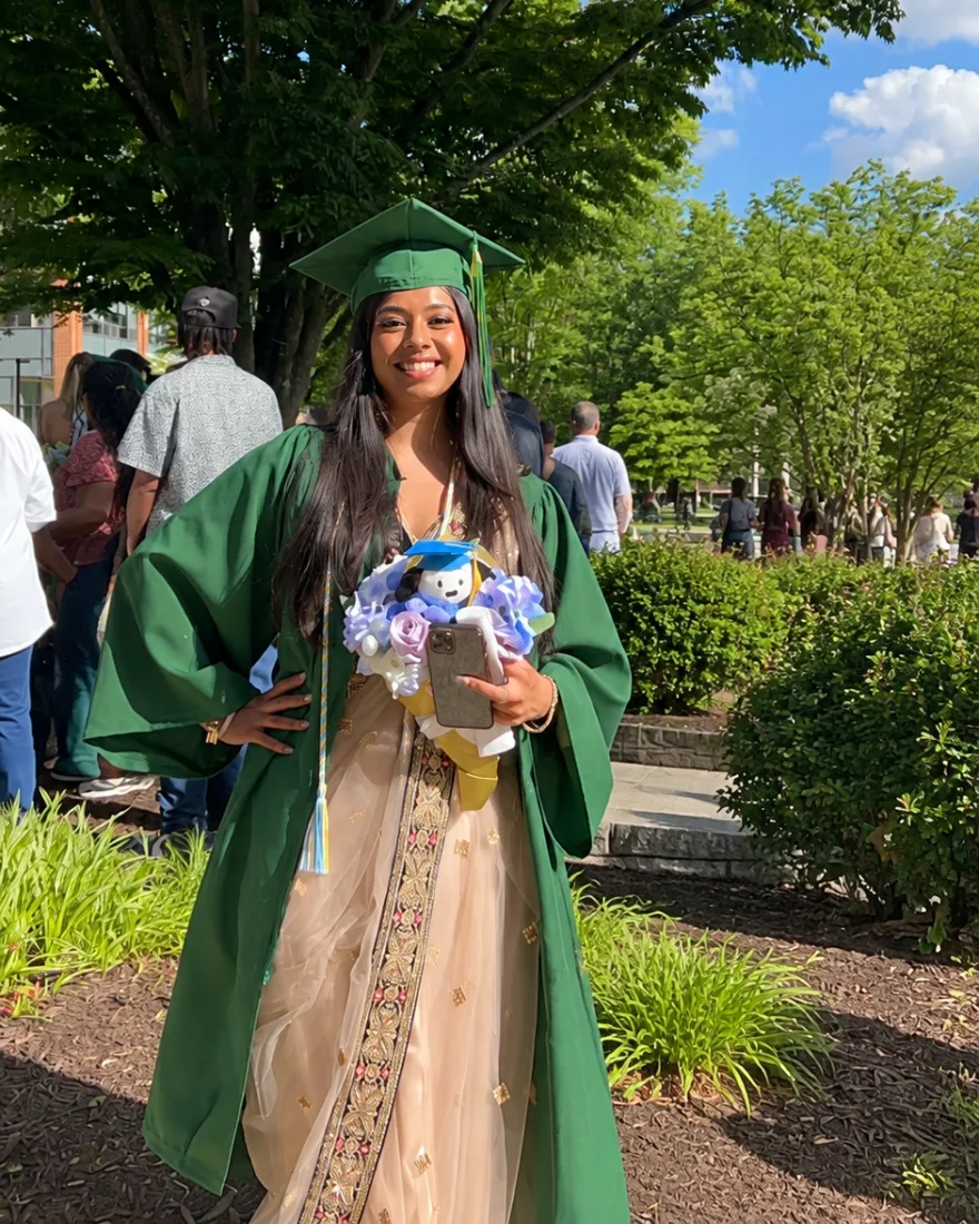 Chanel in her green George Mason cap and gown on graduation day, smiling, with a bouquet
